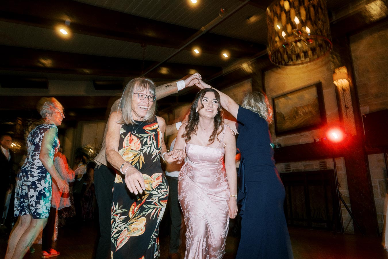 Three women joyfully dancing at a lively indoor celebration, surrounded by soft lighting and a warm atmosphere.