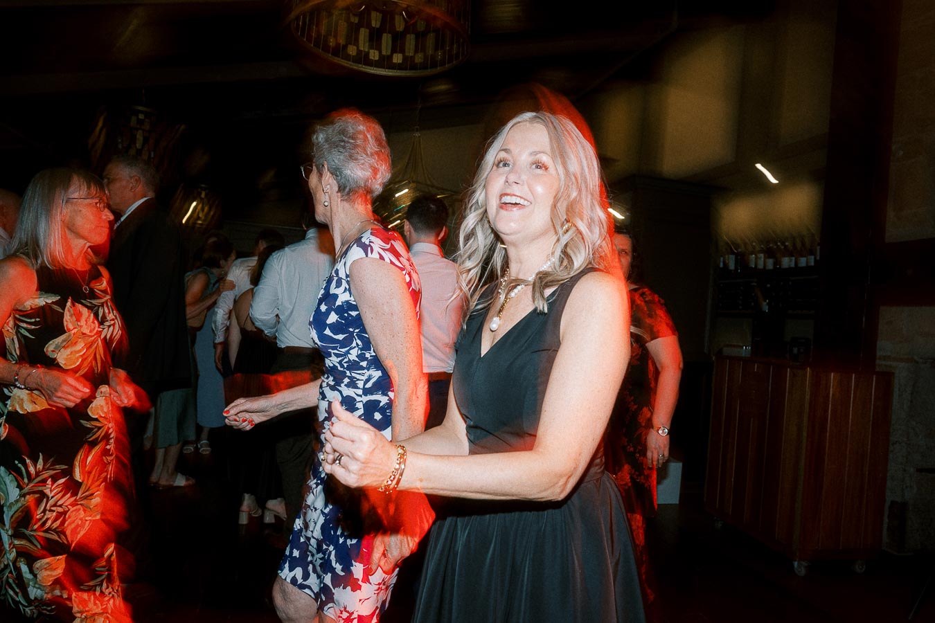 A group of people enjoying a lively dance floor at an indoor party, with vibrant lighting and smiles on their faces.