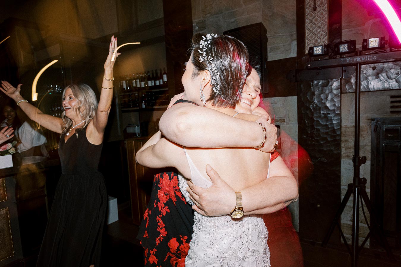 A joyful wedding celebration with guests embracing on the dance floor, wearing elegant dresses.