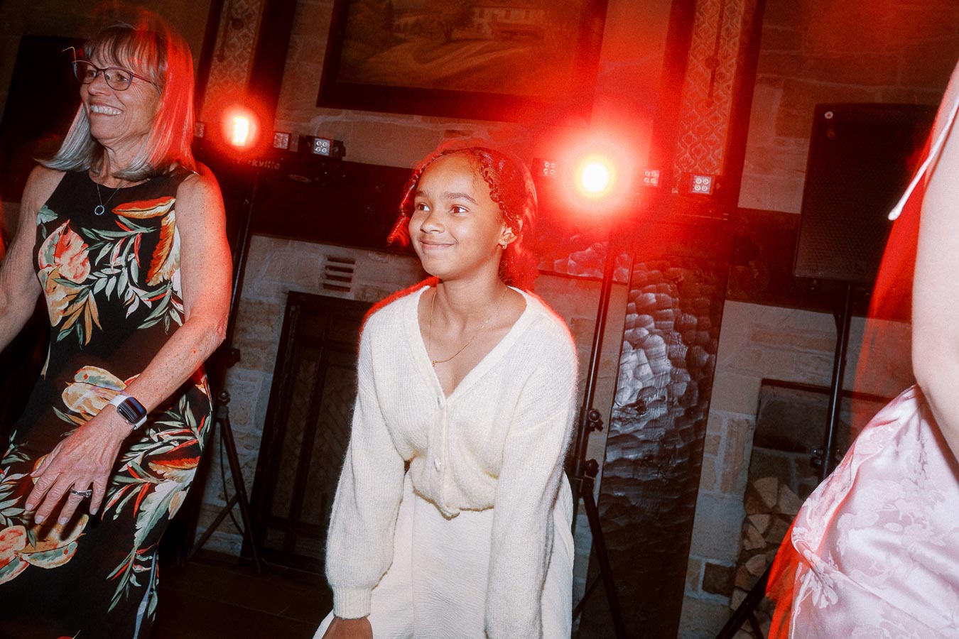 Young girl and older woman dancing at a party with vibrant lighting in the background.