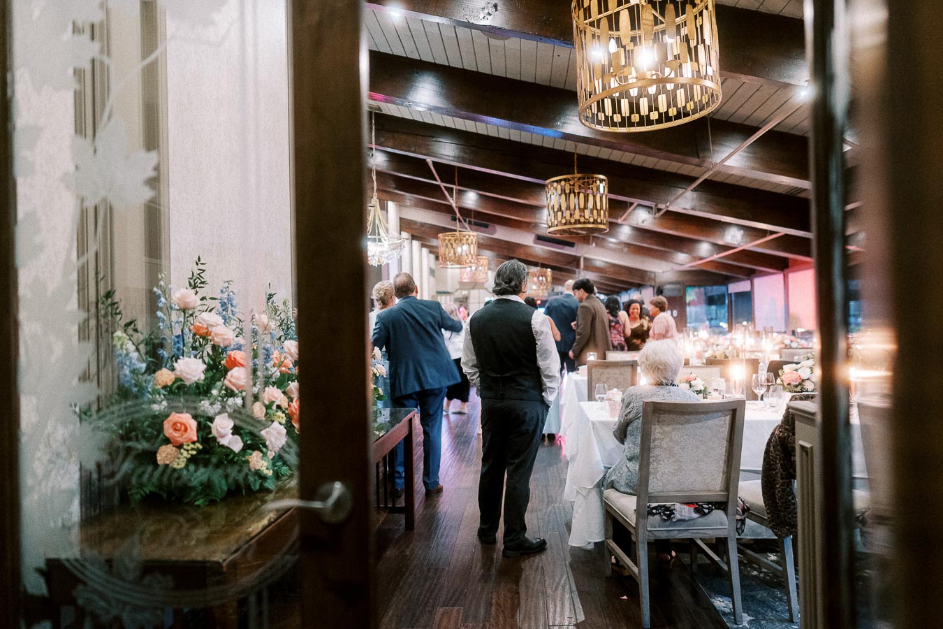 Elegant wedding reception in a beautifully decorated venue with floral arrangements and ambient lighting, guests socializing and dining at tables adorned with candles.
