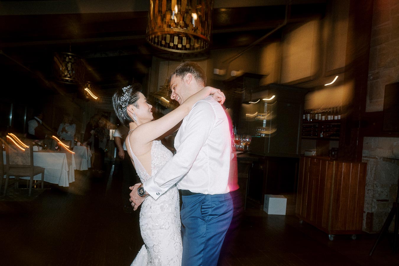 A bride and groom share a romantic first dance in a warmly lit reception hall, surrounded by friends and family celebrating their wedding day.