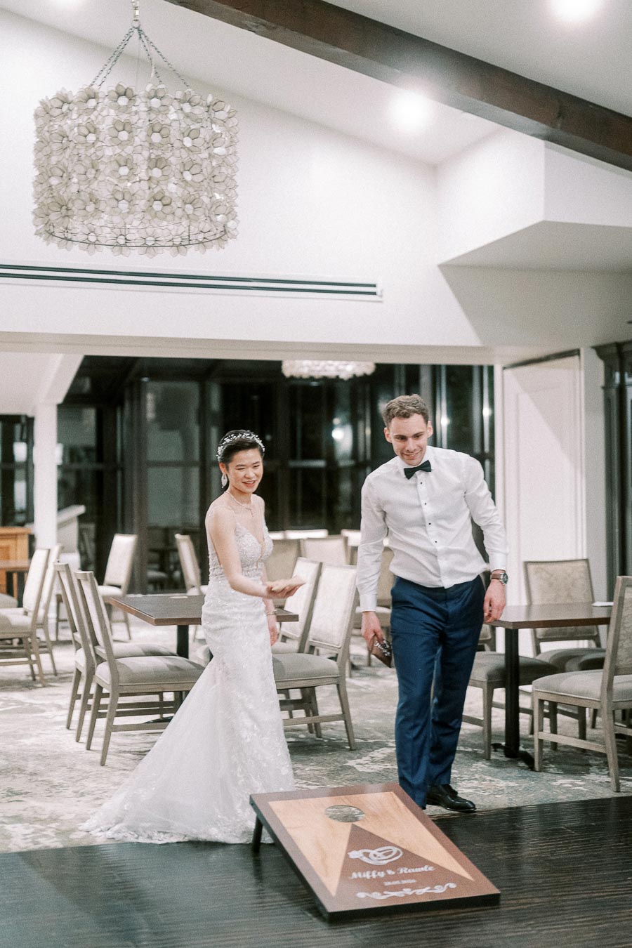 Bride and groom playing cornhole indoors at their wedding reception, adding fun to their elegant celebration.