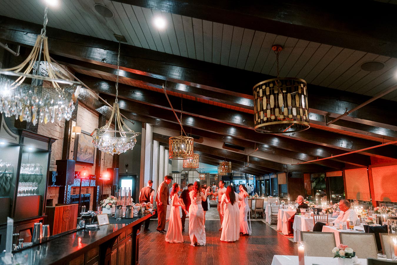Elegant wedding reception with guests dancing in a beautifully decorated venue featuring chandeliers and ambient lighting, complementing the warm and inviting atmosphere.