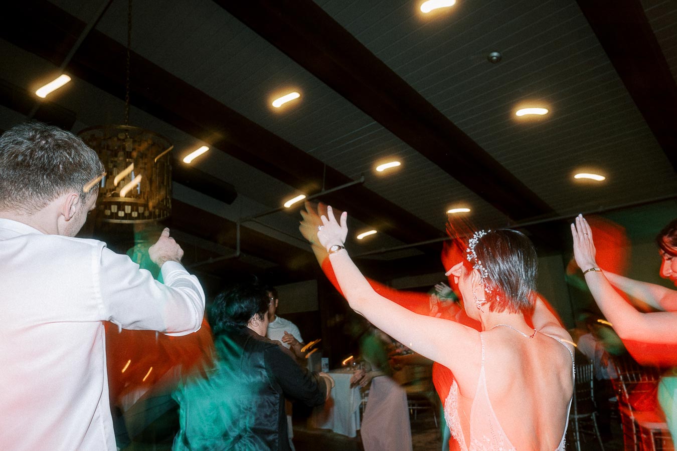 People joyfully dancing at a lively indoor event, with vibrant lights and colorful motion blur, creating a festive atmosphere.