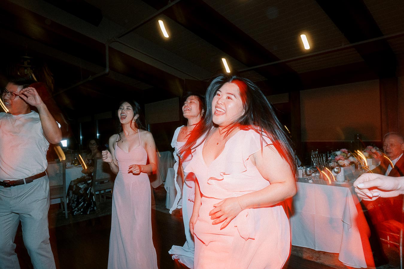 A group of people joyfully dancing and laughing at an indoor party, dressed in elegant attire.