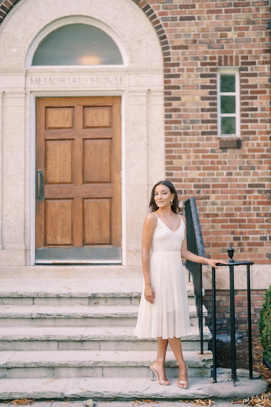 Rachel stands on stone steps beside a black railing in front of Memorial House's brick entrance.