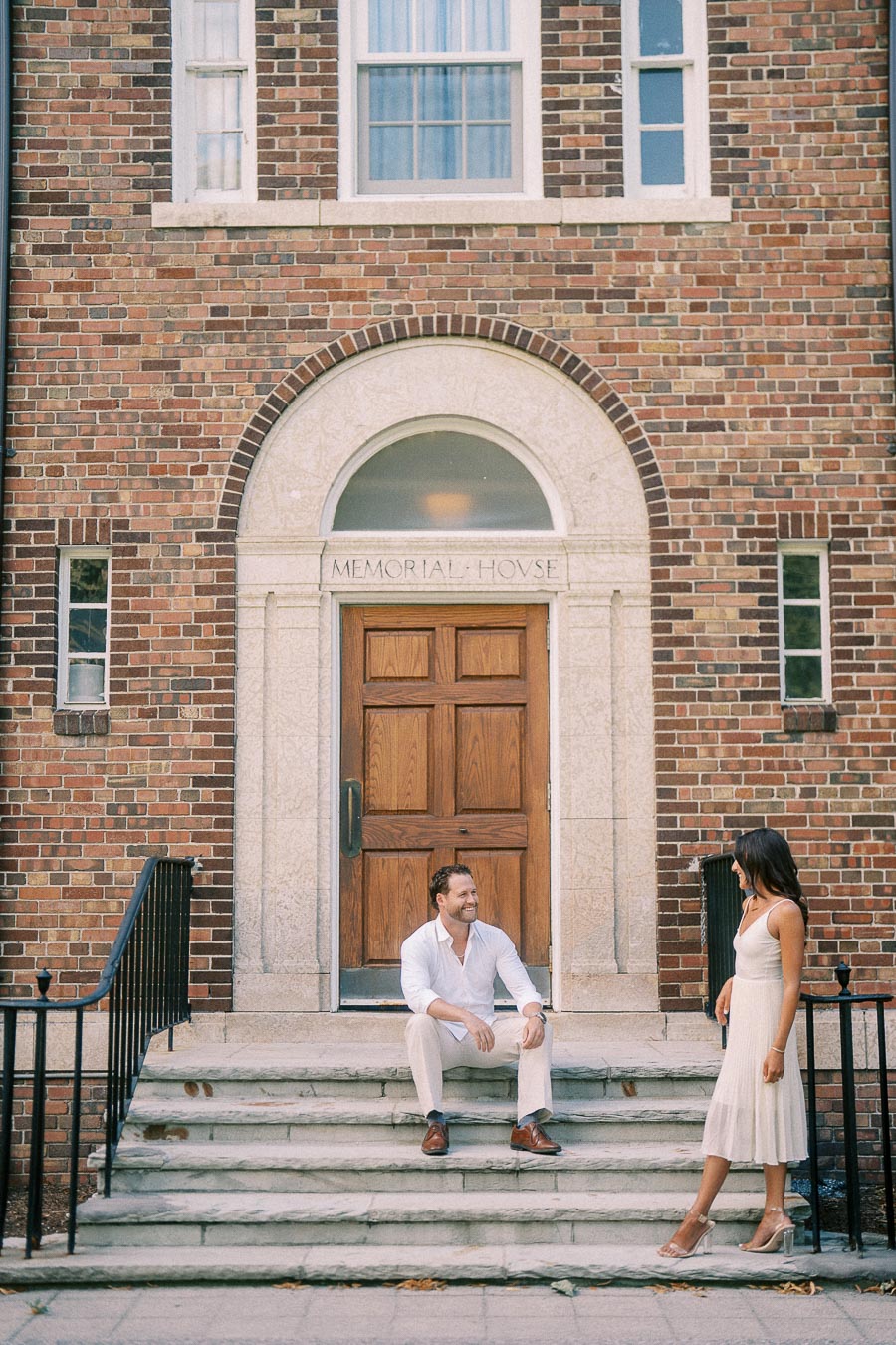 Rachel stands near Matt as he sits on stone steps outside a brick Memorial House entrance in Aurora.