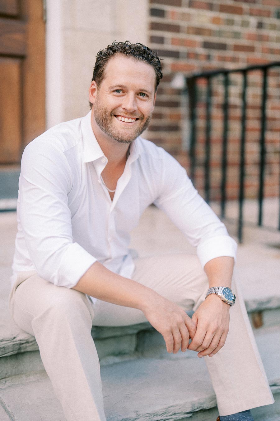 Matt smiles while seated on stone steps beside a brick building in Aurora, Ontario.
