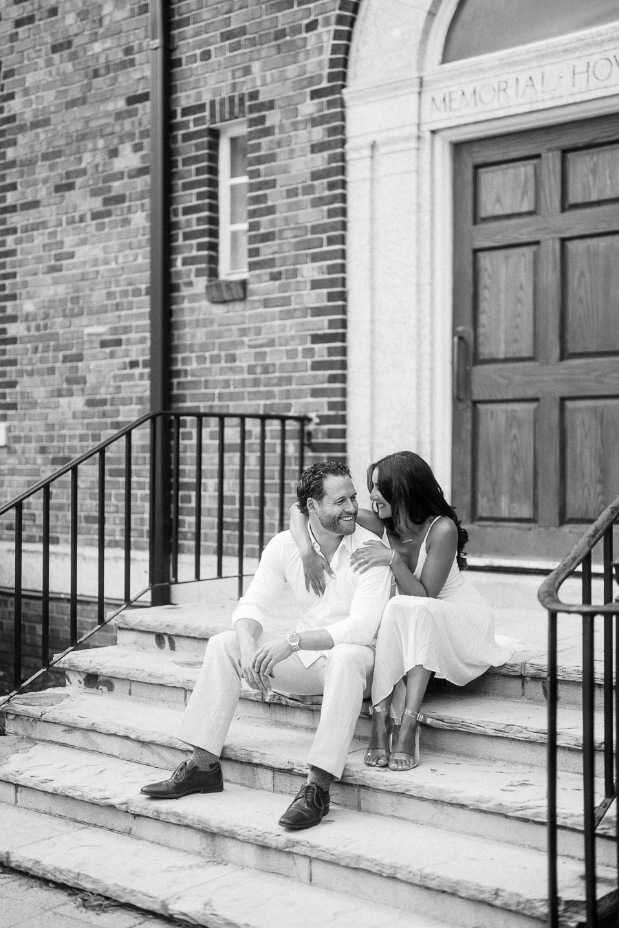 Rachel and Matt sit close together on stone steps outside a brick school entrance, smiling at each other.