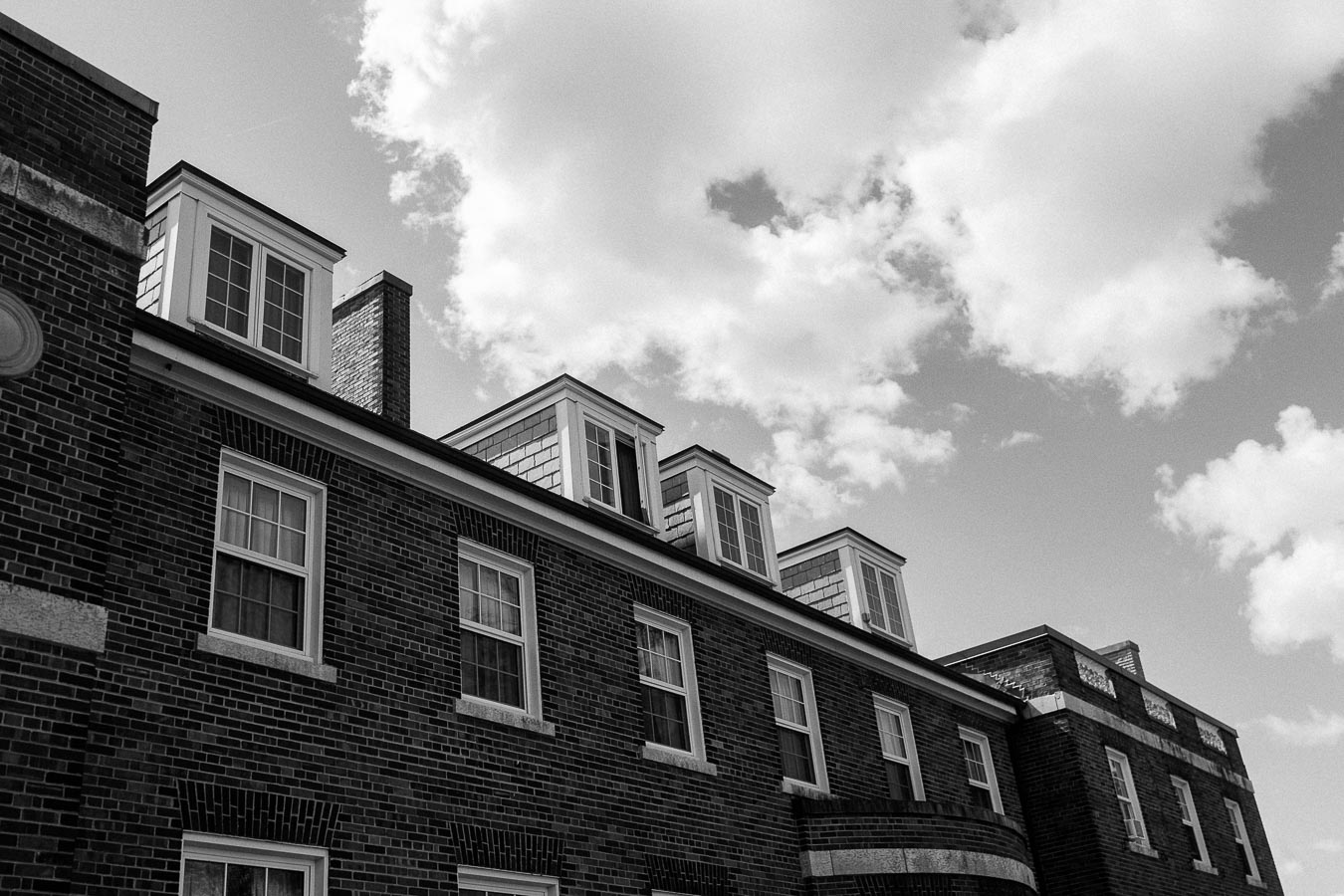 Black-and-white view of a brick campus building with dormer windows beneath a cloudy sky.