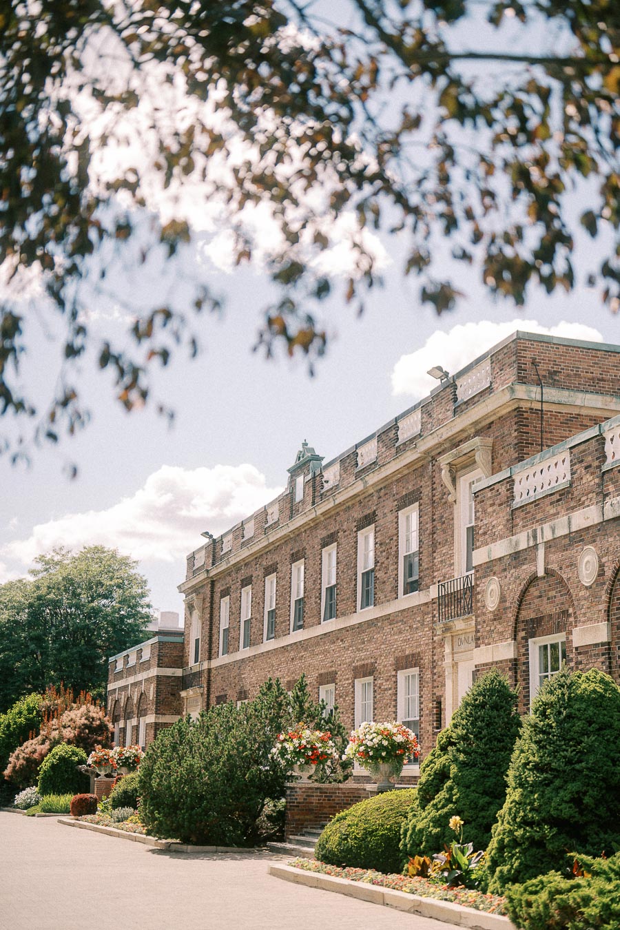 Brick school building in Aurora framed by leafy branches, with gardens and flower planters along the walkway.