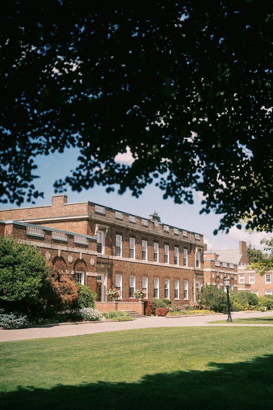 Brick school building with manicured lawn and gardens framed by leafy tree branches in Aurora, Ontario.