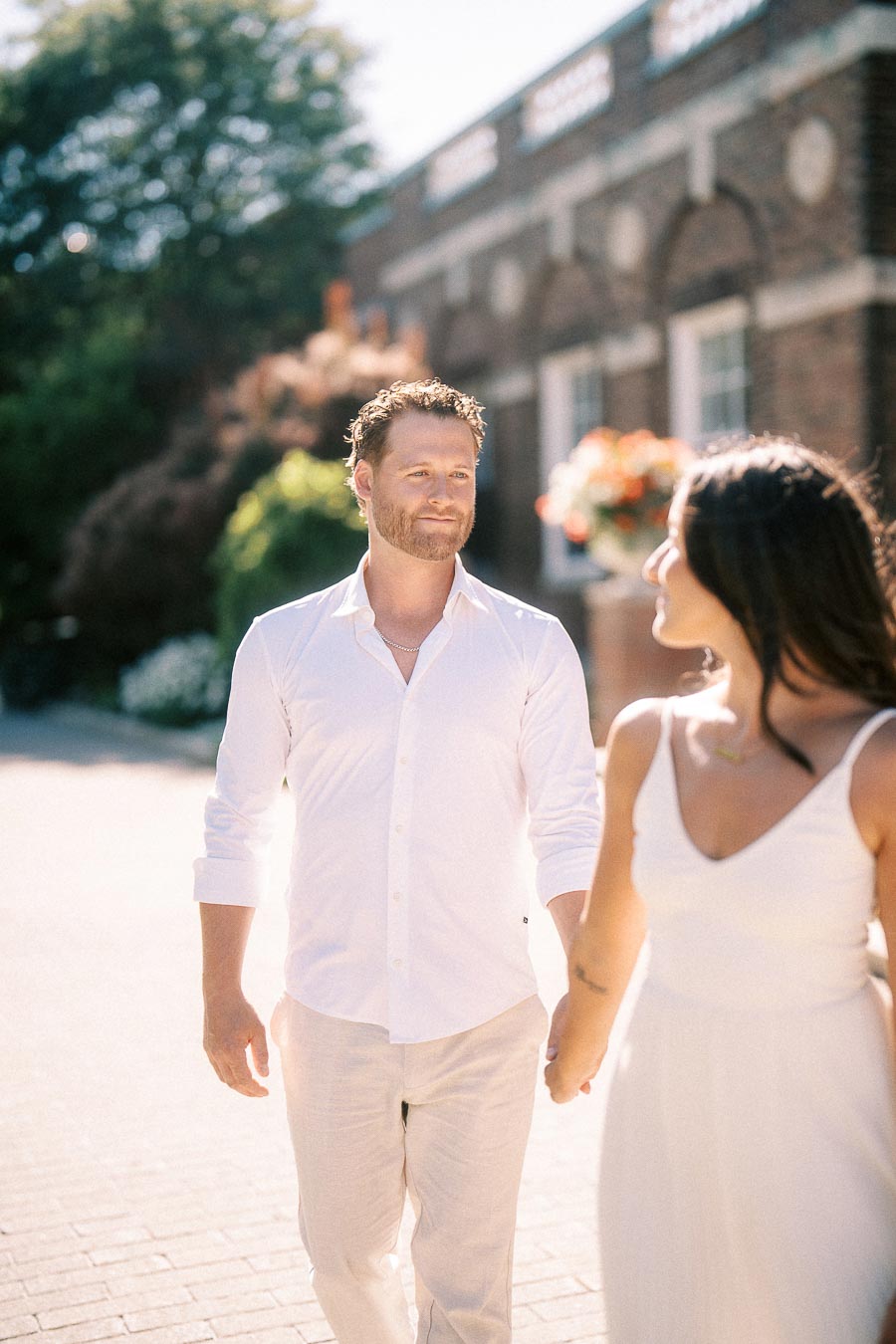 Rachel and Matt hold hands while walking past a brick building in sunny Aurora, Ontario.