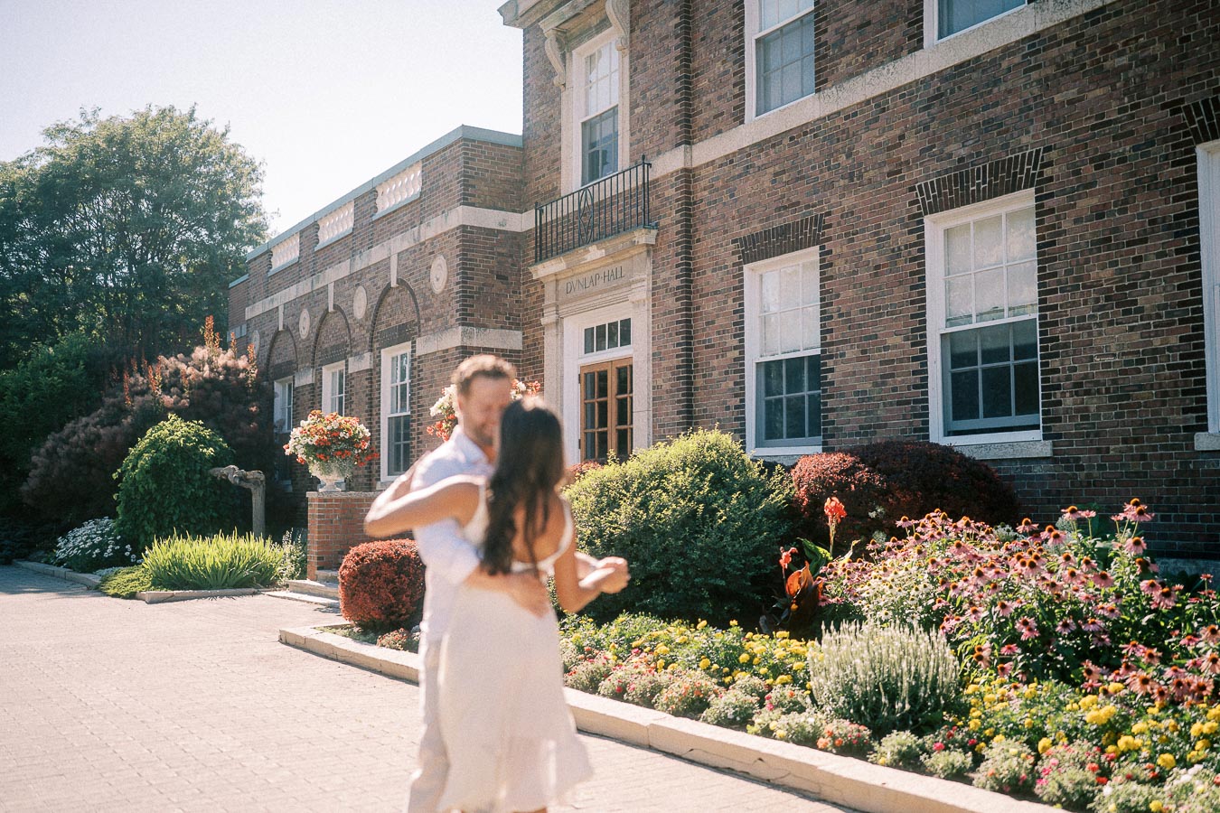 Rachel and Matt embrace beside flower beds outside Dunlap Hall at St. Andrew’s College.