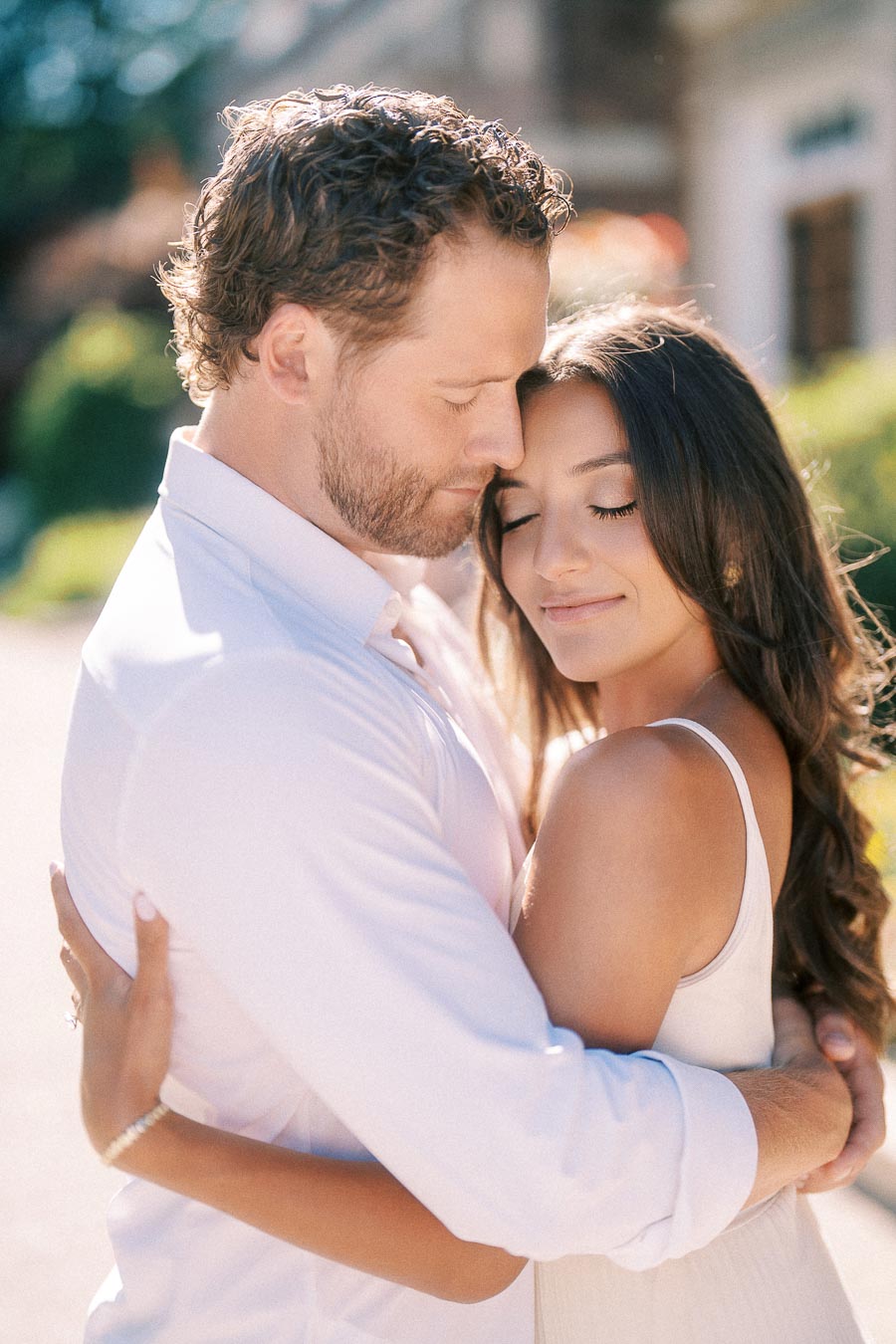 Rachel and Matt embrace outdoors in bright sunlight, eyes closed in a quiet engagement portrait.