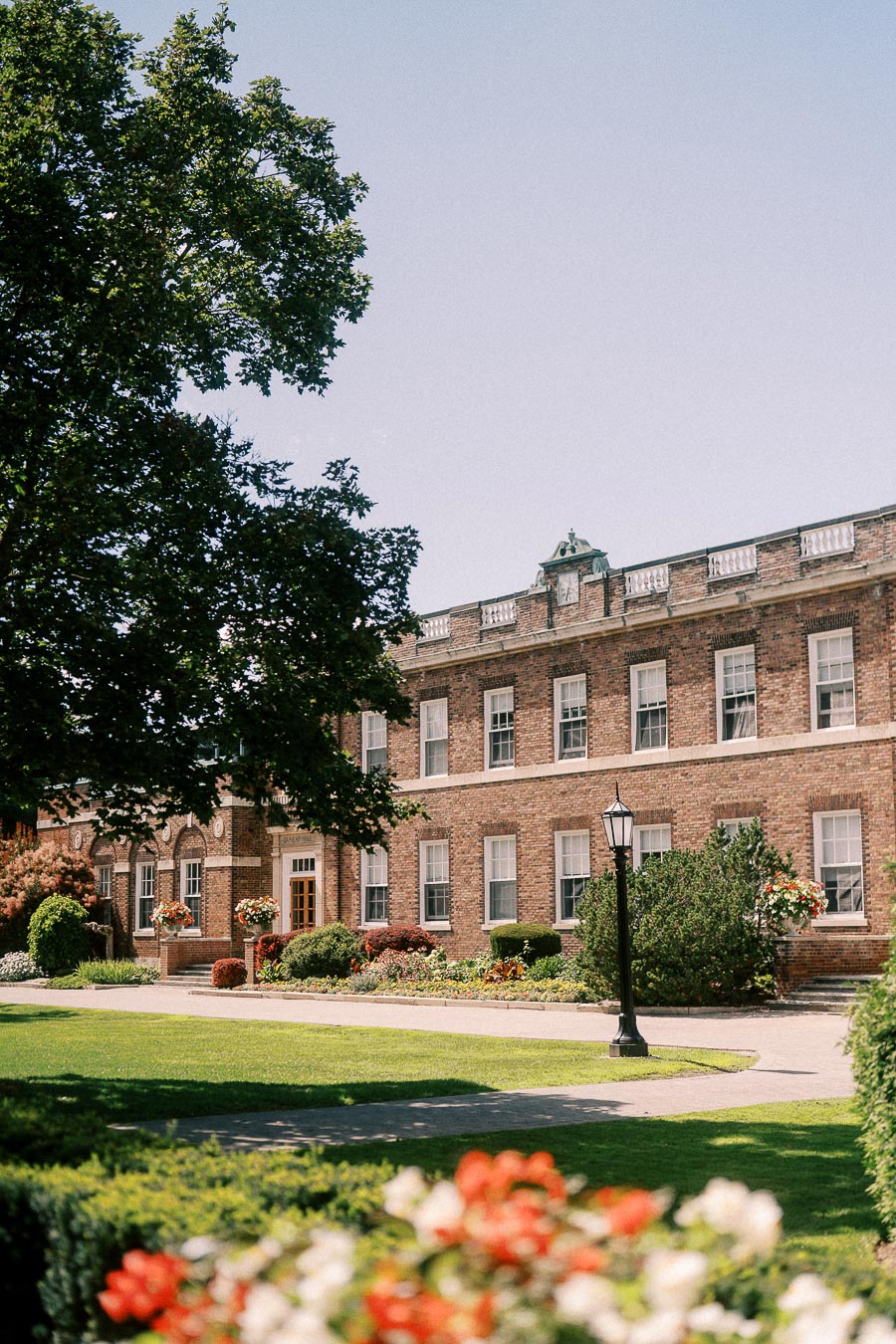 Brick campus building with gardens, lawn, trees, and a black lamppost in Aurora, Ontario.
