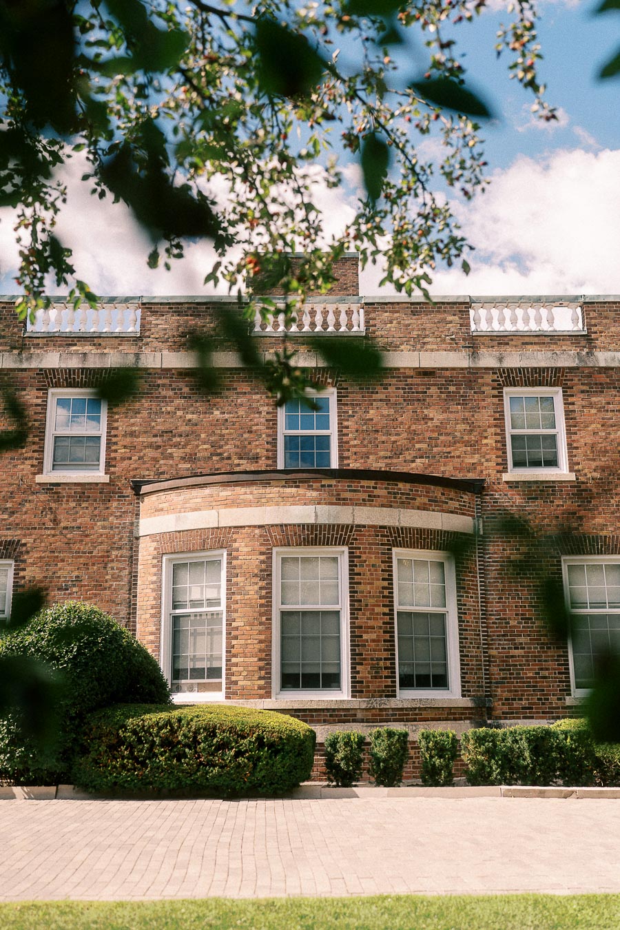 Brick campus building with tall windows and hedges seen through leafy branches in Aurora, Ontario.