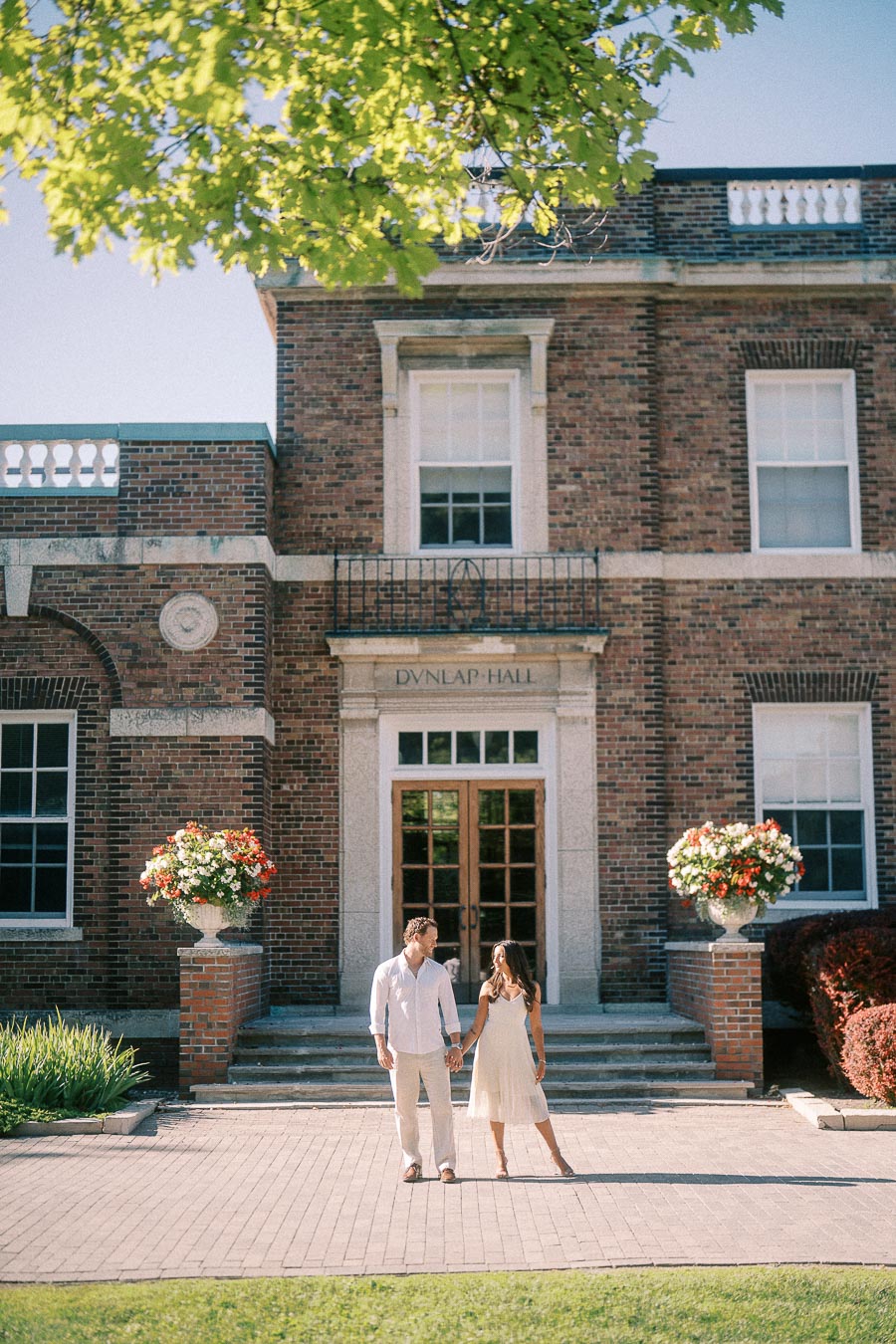 Rachel and Matt hold hands in front of Dunlap Hall's brick entrance at St. Andrew's College.