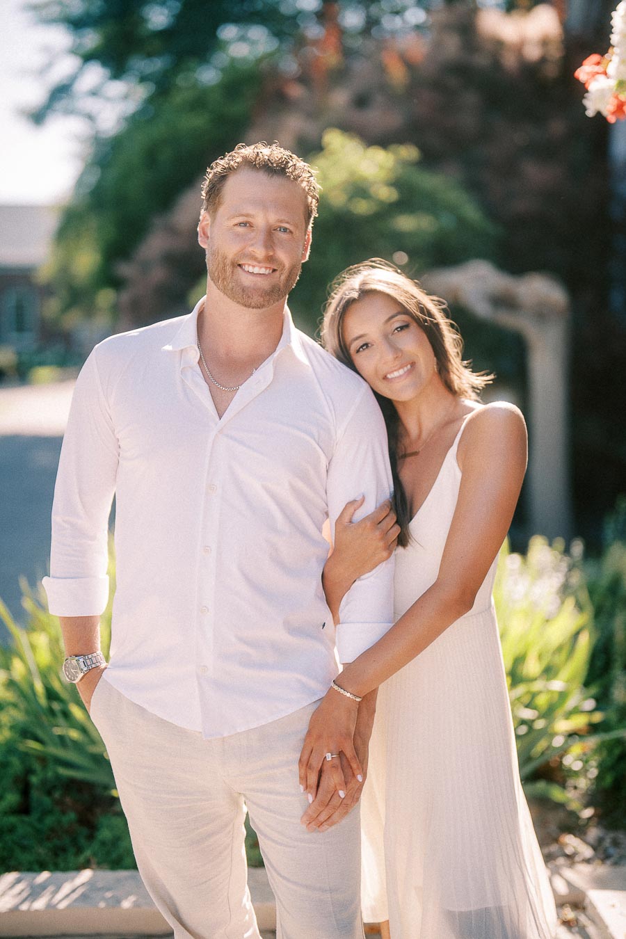 Rachel leans against Matt as they smile together in bright summer light on a landscaped path.
