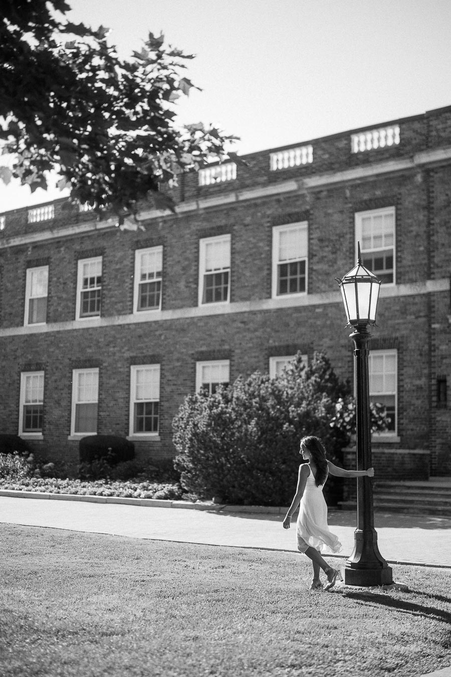 Rachel stands beside a lamp post on a lawn in front of a brick school building in Aurora, Ontario.