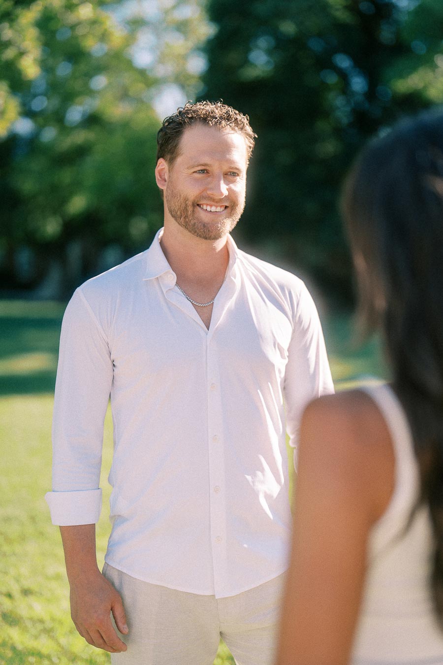 Matt smiles at Rachel on a sunny lawn, with trees softly blurred behind him in Aurora, Ontario.