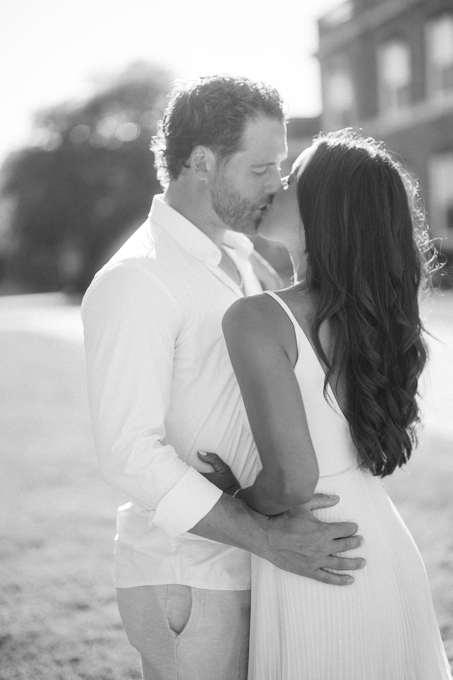 Rachel and Matt kiss while standing close together outdoors in soft sunlight in Aurora, Ontario.