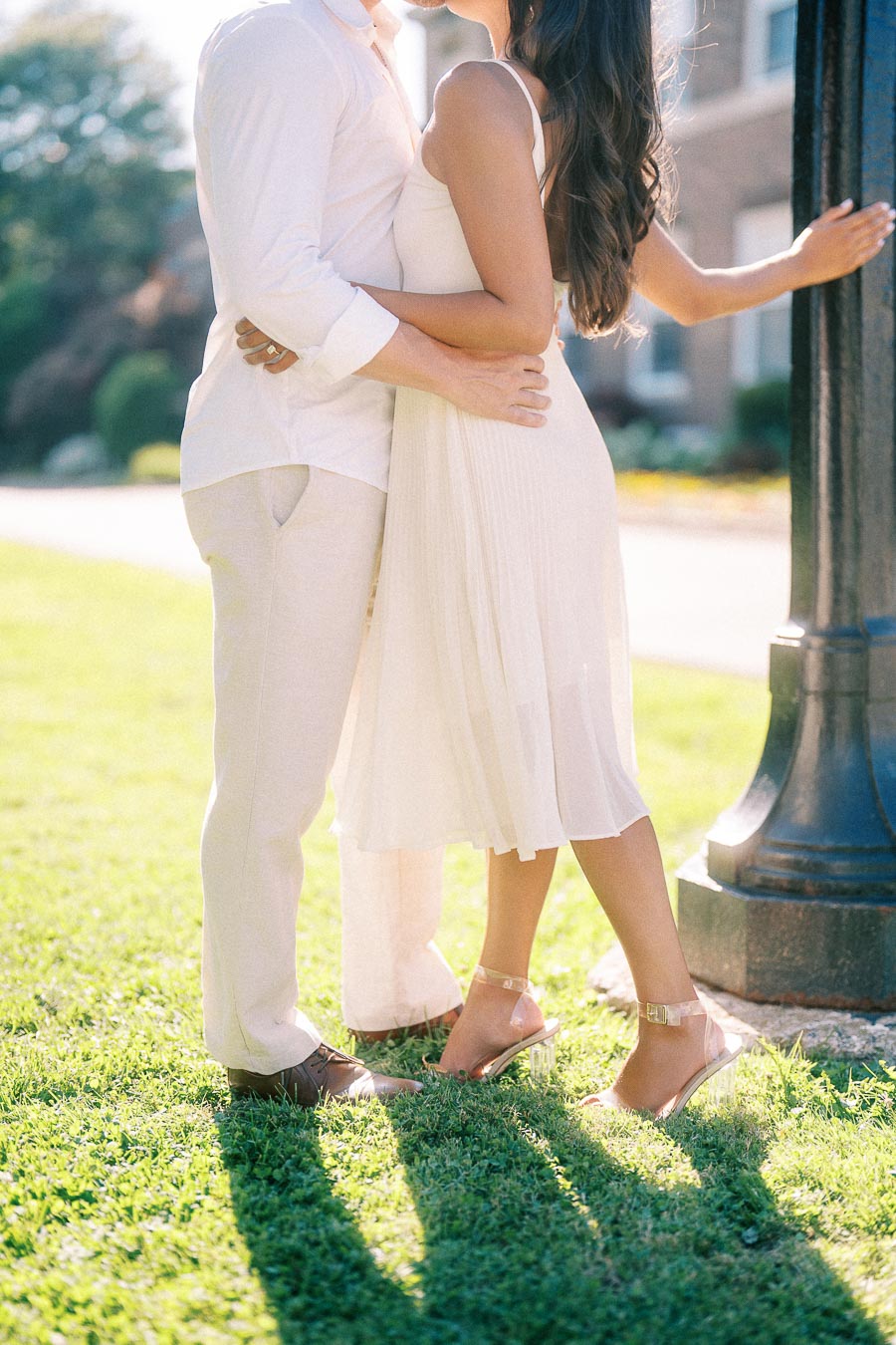 Rachel and Matt embrace on sunlit grass beside a lamppost during their Aurora engagement session.