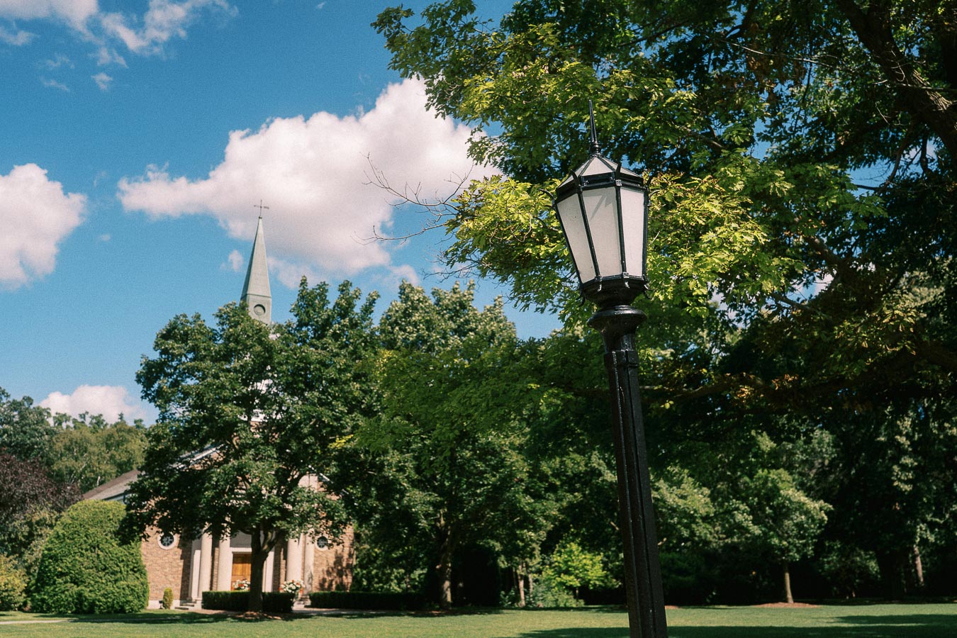 Lamp post and church steeple rise above leafy grounds under a bright summer sky in Aurora, Ontario.