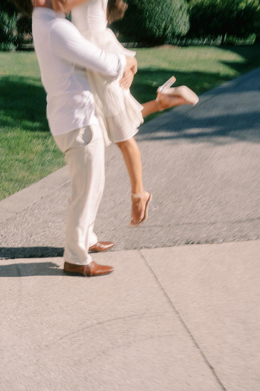 Matt lifts Rachel on a sunlit path as her dress and heels move in a playful engagement moment.