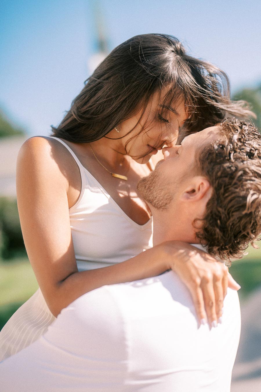 Rachel and Matt share a close embrace outdoors, touching noses in bright summer light.