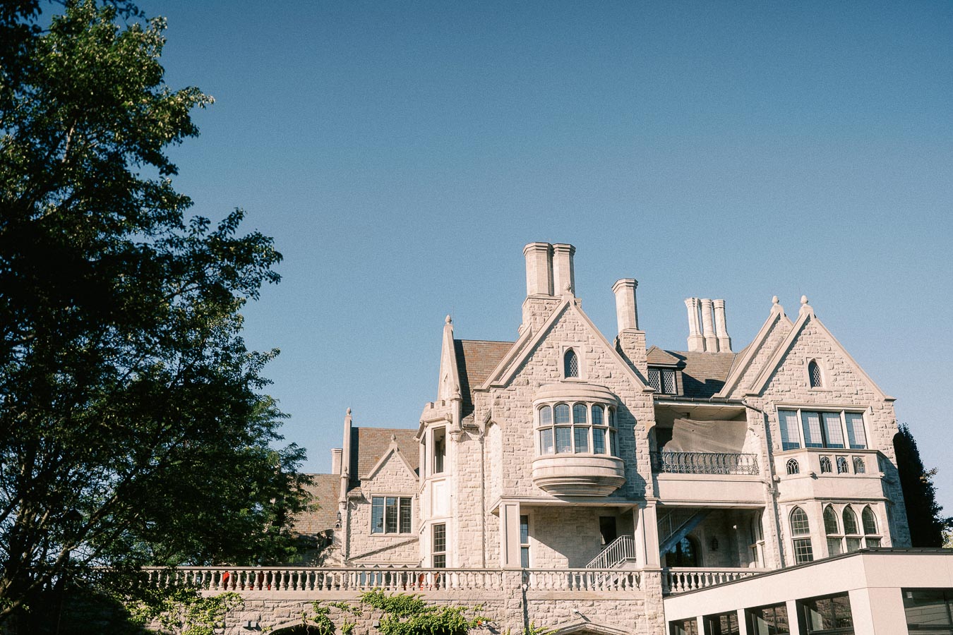 Stone collegiate building with gables and chimneys under a clear sky, framed by trees in Aurora, Ontario.