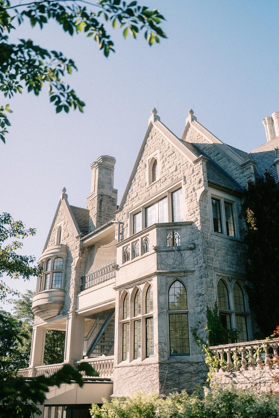 Sunlit stone campus building with gables, arched windows, balconies, and trees in Aurora, Ontario.