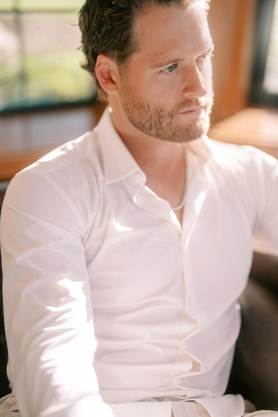 Matt sits indoors in a white shirt, looking away as warm window light falls across his face.