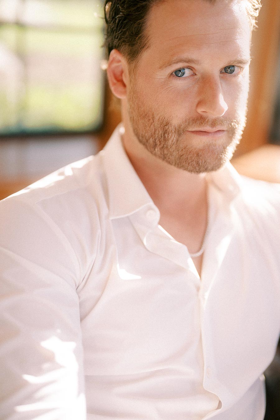 Matt sits in warm window light wearing a white shirt, looking toward the camera in a close portrait.