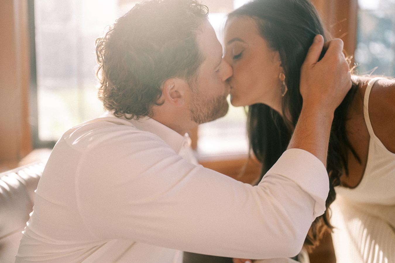 Rachel and Matt kiss indoors beside sunlit windows as Matt gently holds her hair.