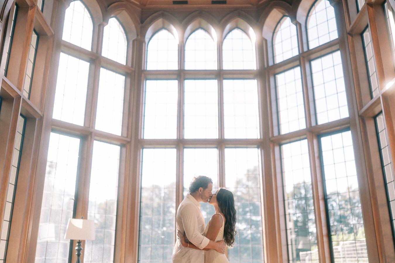 Rachel and Matt kiss in front of tall arched windows inside a bright hall in Aurora, Ontario.