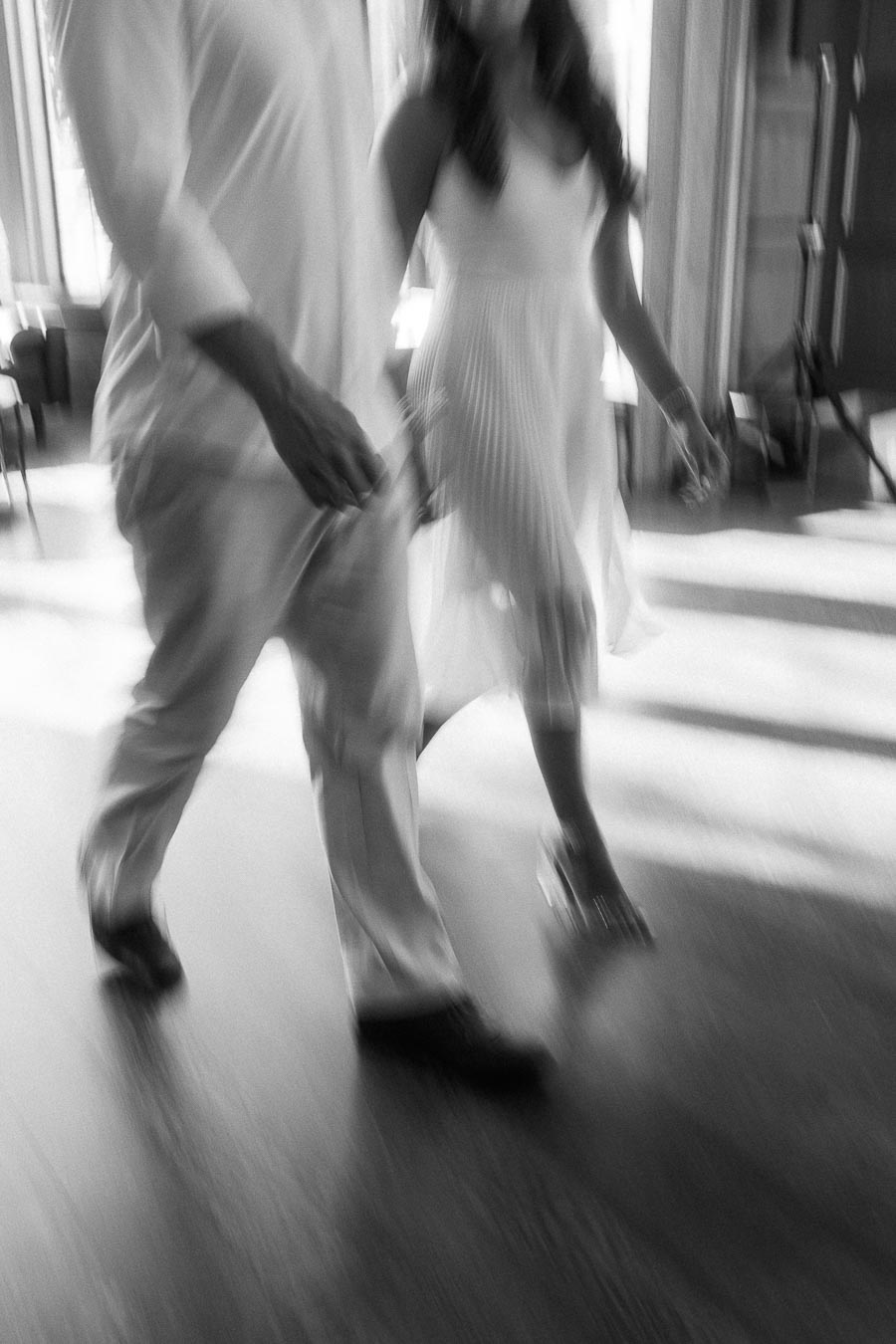 Rachel and Matt walk hand in hand through a sunlit interior, captured with soft motion blur.