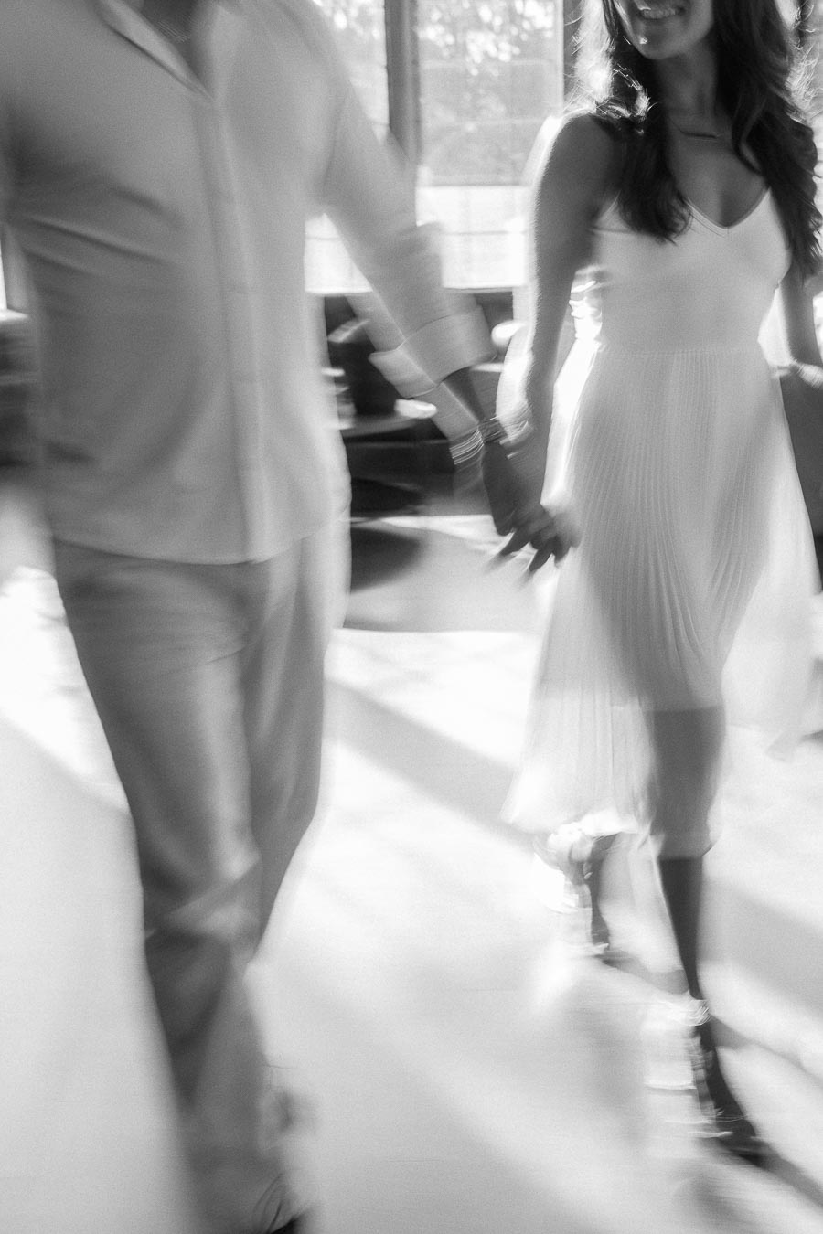 Rachel and Matt hold hands while walking through a bright indoor space with soft motion blur.