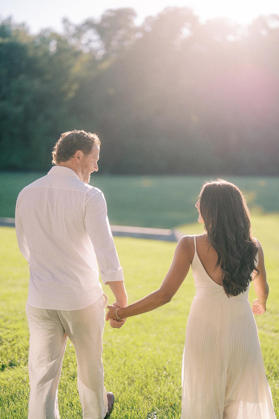 Rachel and Matt hold hands while walking across a sunlit grassy field in Aurora, Ontario.