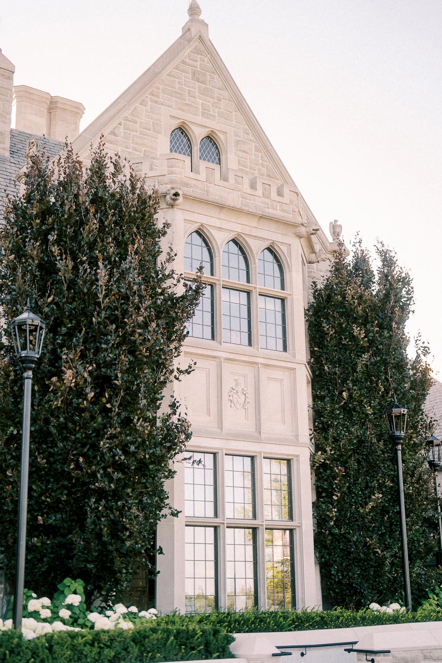 Gothic-style stone building with tall windows, ivy, hedges, white flowers, and lampposts in Aurora.