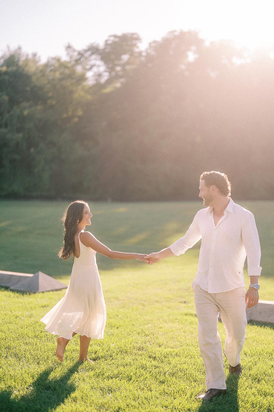 Rachel and Matt hold hands and smile while walking through a sunlit grassy field in Aurora, Ontario.