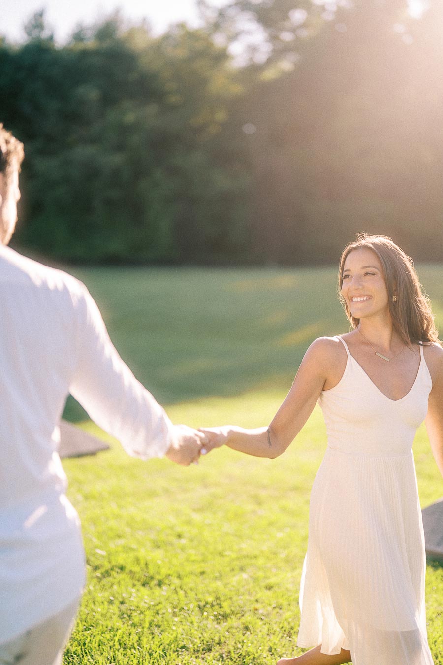 Rachel smiles while holding Matt’s hand in a sunlit grassy field in Aurora, Ontario.