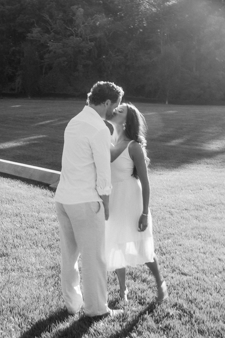 Rachel and Matt kiss on a sunlit grassy field with trees in the background in Aurora, Ontario.