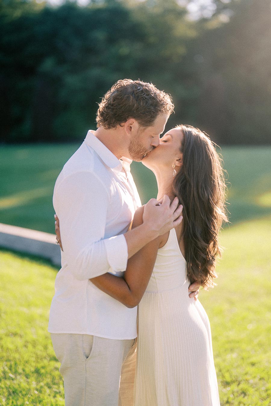 Rachel and Matt kiss while standing close together on a sunny lawn in Aurora, Ontario.