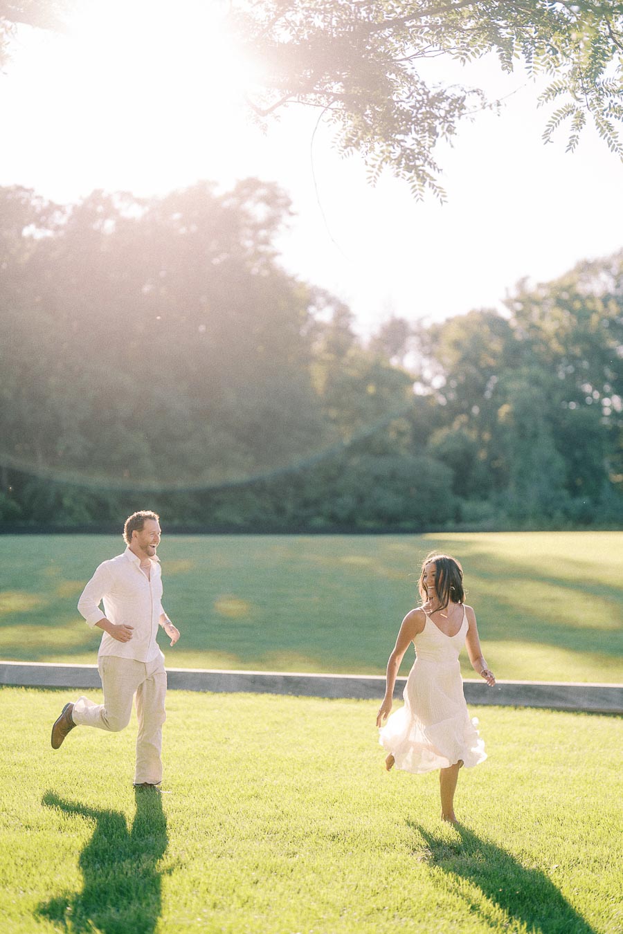 Rachel and Matt run across a sunlit grassy field, smiling in warm evening light in Aurora, Ontario.