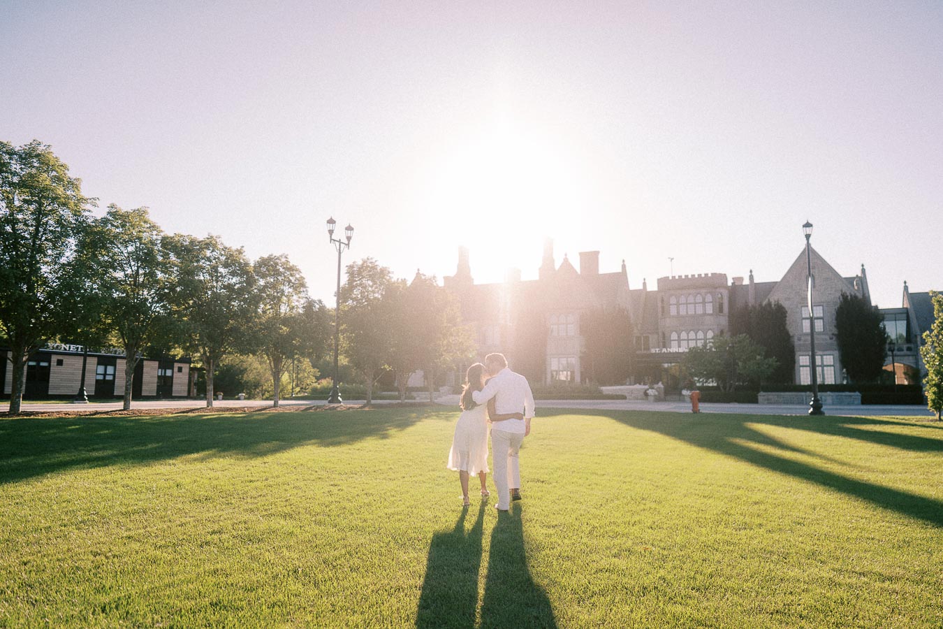 Rachel and Matt walk arm in arm across a sunny lawn toward a school building in Aurora, Ontario.