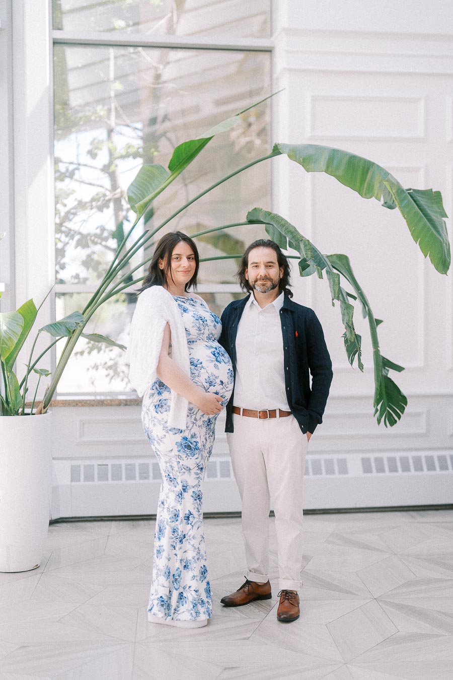 Pregnant woman and man posing beside large tropical plants indoors