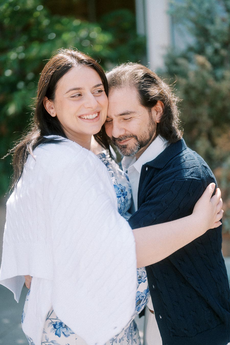 Smiling pregnant woman embraces man outdoors in soft sunlight