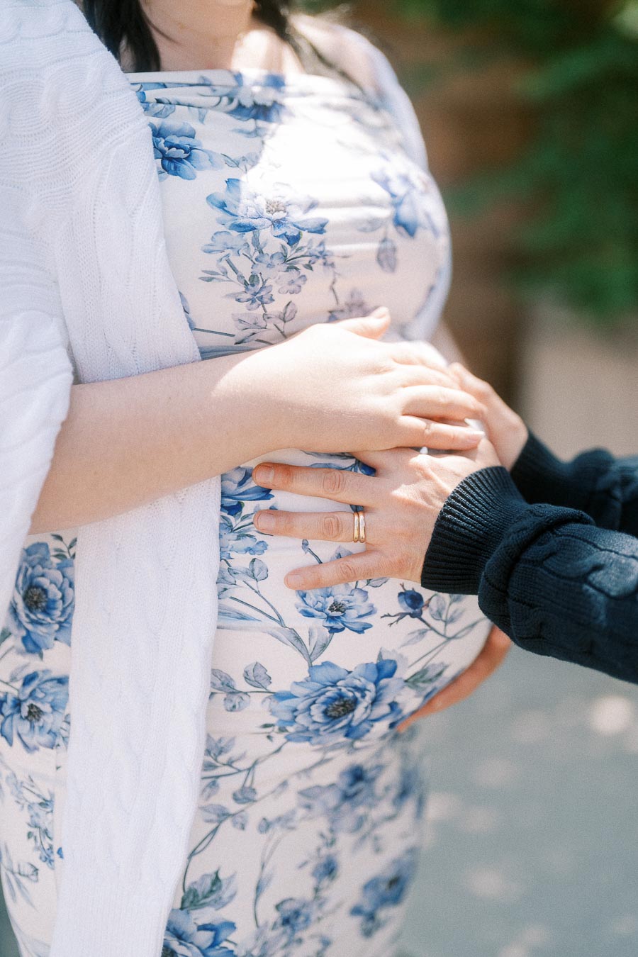 Hands resting on a pregnant belly in a blue floral dress